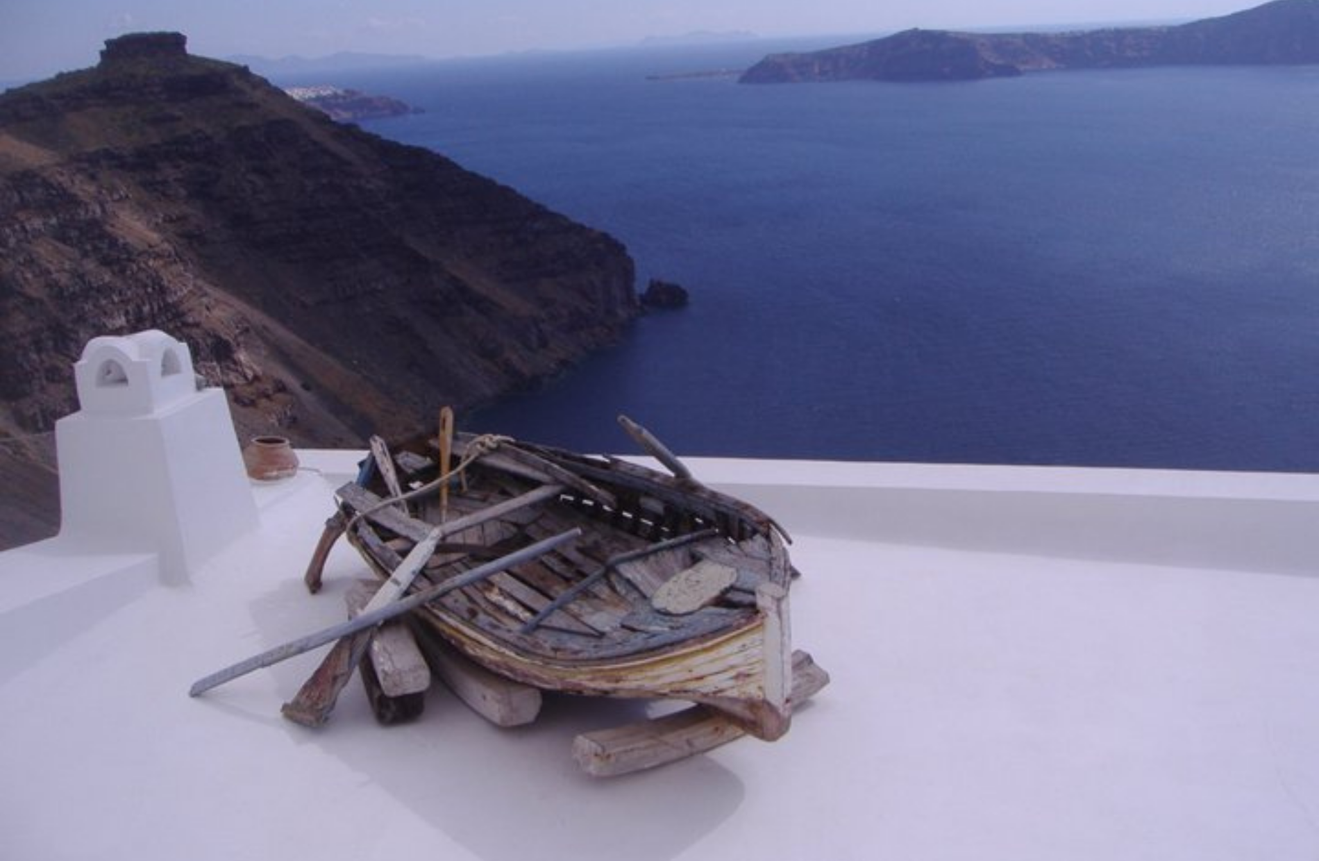 an ancient wooden boat on the top of a white roof overseeing the sea and mountainside in the background